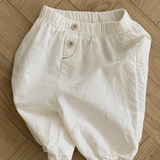 Auf einem Holzboden ist eine weiße Bebe Holic Natural Pants mit elastischem Bund und Knopfverschluss abgebildet. Die Hose hat eine lockere, bequeme Passform mit elastischen Beinöffnungen und ist damit ein vielseitiges Must-have für die Garderobe jedes Babys.