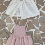 Auf einem gemusterten Steinboden sind drei Kinderkleider von Bebe Holic ausgestellt: zwei in Hellbeige und eines in Zartrosa, alle in schlichtem, elegantem Design, aus leichten Stoffen.