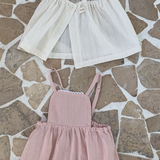 Auf einem gemusterten Steinboden sind drei Kinderkleider von Bebe Holic ausgestellt: zwei in Hellbeige und eines in Zartrosa, alle in schlichtem, elegantem Design, aus leichten Stoffen.