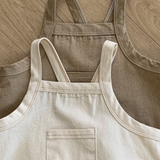 Zwei Twill-Bodysuits mit Taschen von Bebe Holic liegen auf einem hellen Fischgrätmusterboden aus Holz. Ein Bodysuit ist hellbeige mit einer kleinen Vordertasche, der andere ist dunkler beige und hat eine schlichte Vorderseite. Beide Bodysuits sind aus weicher Baumwolle gefertigt und haben verstellbare Träger für eine einfache Anpassung.