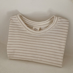 Ein ordentlich gefaltetes, beige-weiß gestreiftes Langarmshirt mit der Aufschrift „Basic ST Tee“ von Bebe Holic liegt auf einer weißen Fläche. Dieses gestreifte Baby-T-Shirt verströmt klassischen Stil, wobei sein schlichter, heller Hintergrund die Einfachheit und Sauberkeit des Designs unterstreicht.