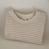 Ein ordentlich gefaltetes, beige-weiß gestreiftes Langarmshirt mit der Aufschrift „Basic ST Tee“ von Bebe Holic liegt auf einer weißen Fläche. Dieses gestreifte Baby-T-Shirt verströmt klassischen Stil, wobei sein schlichter, heller Hintergrund die Einfachheit und Sauberkeit des Designs unterstreicht.