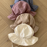 Fünf Crunch Bucket Hats in einer natürlichen Farbpalette (Blau, Rosa, Braun, Beige und Creme) sind ordentlich auf einem hölzernen Boden im Fischgrätenmuster gestapelt. Der cremefarbene Hut oben hat zwei dünne Riemen. Entdecken Sie die bezaubernde Auswahl von Bebe Holic für Ihre Kleinen.