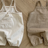 Zwei Twill-Bodysuits mit Taschen von Bebe Holic, einer weiß und einer beige, liegen flach auf einem Holzboden. Jeder hat eine Tasche auf der Vorderseite.