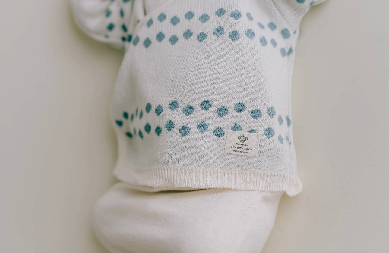 Nahaufnahme eines Baby-Stramplers „Pack Dots Jeans für Neugeborene“ mit einem Muster aus blauen Punkten und einem sichtbaren Micu-Micu-Etikett auf hellem Hintergrund, aus 100 % Bio-Baumwolle.
