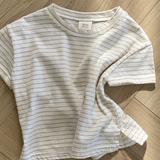 Ein weißes kurzärmliges Basic ST Tee mit dünnen schwarzen Querstreifen von Bebe Holic liegt ordentlich auf einem Holzboden mit Fischgrätenmuster und zeigt seinen klassischen Stil. Der Stoff des T-Shirts ist leicht zerknittert.