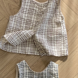 Zwei ärmellose, karierte Westen aus gestepptem Stoff werden auf einem Holzboden ausgestellt. Die obere Weste aus der Summer Check Sleeveless Tee-Kollektion von Bebe Holic hat ein braun-weißes Muster mit Knöpfen auf der Vorderseite, während die untere Weste ein schwarz-weißes Muster ohne sichtbare Knöpfe aufweist, was modisches Flair verleiht.