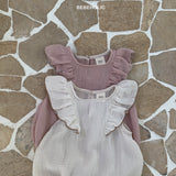 Zwei Bebe Holic Lily Wing Body Suits auf einem Steinuntergrund präsentiert, einer in Pink mit romantischen Rüschen an den Ärmeln und einer in Beige mit einem Rü.