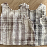 Zwei Summer Check Sleeveless Tees von Bebe Holic aus strukturiertem Stoff mit Gittermuster liegen auf einem Holzboden. Ein Oberteil ist weiß mit rotem Gitter, das andere weiß mit schwarzem Gitter. Jedes Oberteil hat eine kleine Tasche auf der Brust, die einen Hauch modischen Flairs verleiht und perfekt in jede Bebeholic-Kollektion passt.