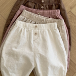 Vier Paar Natural Pants für Kinder von Bebe Holic liegen ordentlich gestapelt auf einem Holzboden. Diese vielseitigen Must-have-Shorts sind in den Farben Braun, Rosa, Beige und Weiß erhältlich und verfügen jeweils über eine elastische Taille und einen Knopf in der Mitte vorne.