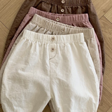 Vier Paar Natural Pants für Kinder von Bebe Holic liegen ordentlich gestapelt auf einem Holzboden. Diese vielseitigen Must-have-Shorts sind in den Farben Braun, Rosa, Beige und Weiß erhältlich und verfügen jeweils über eine elastische Taille und einen Knopf in der Mitte vorne.