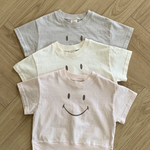 Drei kurzärmlige Bebe Holic Smile T-Shirts liegen ordentlich gestapelt auf einem Holzboden. Das obere Shirt ist hellgrau, das mittlere ist cremefarben und das untere ist hellrosa. Jedes dieser Kinder-T-Shirts aus weicher Baumwolle hat auf der Vorderseite ein einfaches Smiley-Design.